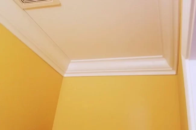 basement-crown-molding-detail-aspect-ratio-960-640 Close-up of white crown molding installed along the ceiling above yellow basement walls