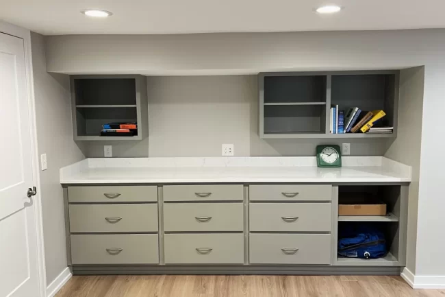 basement-storage-cabinets-countertop-scaled-aspect-ratio-960-640 Built-in basement storage cabinets with drawers, open shelving, white countertop, and light wood-look flooring