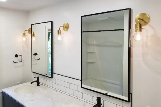bathroom-mirror-and-lighting-update-aspect-ratio-960-640 Bathroom vanity area with black framed mirrors, updated wall lighting, white tile backsplash, and black fixtures