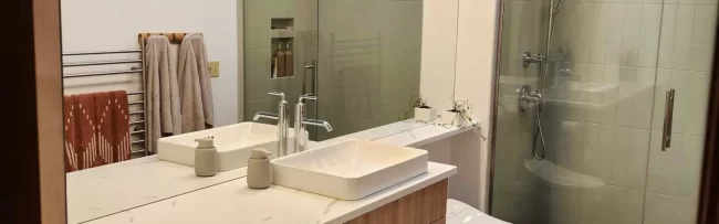 bathroom-vanity-shower-hero-1-aspect-ratio-1920-600 Updated bathroom with wood vanity, white countertop, vessel sink, large mirror, and glass shower door