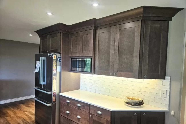 custom-kitchen-cabinetry-storage-aspect-ratio-960-640 Custom dark wood kitchen cabinetry with crown molding, built-in microwave, white countertop, and subway tile backsplash