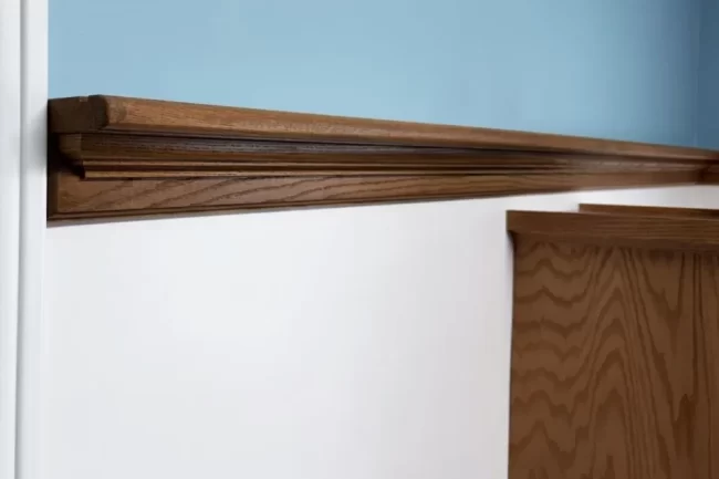 custom-wood-picture-rail-trim-aspect-ratio-960-640 Close-up of custom stained wood picture rail trim installed above a white wall and doorway