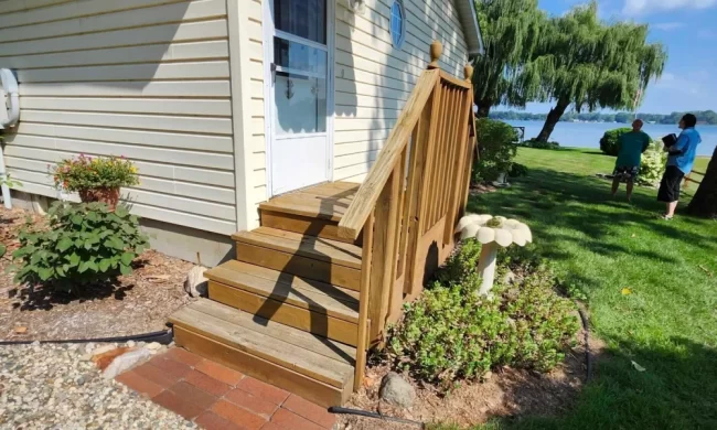 Before view of exterior deck stairs with older wood railings leading from the side entry toward the lakeside yard