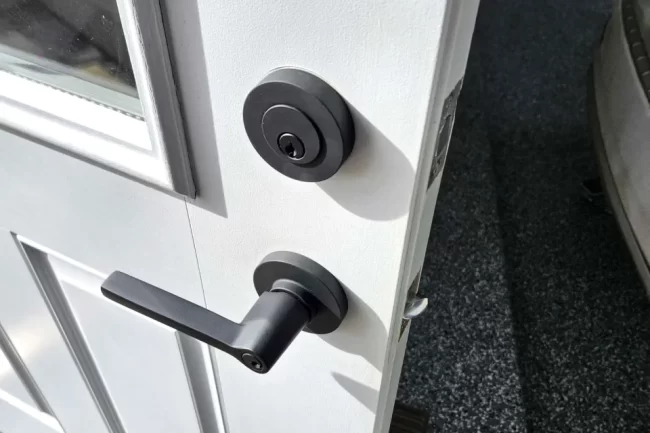 Close-up of black front door hardware with a deadbolt and handle installed on a white exterior door