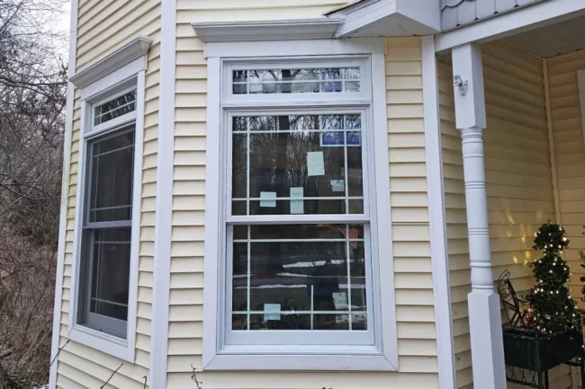 Replacement double-hung windows with white trim on a home with yellow siding and a covered porch