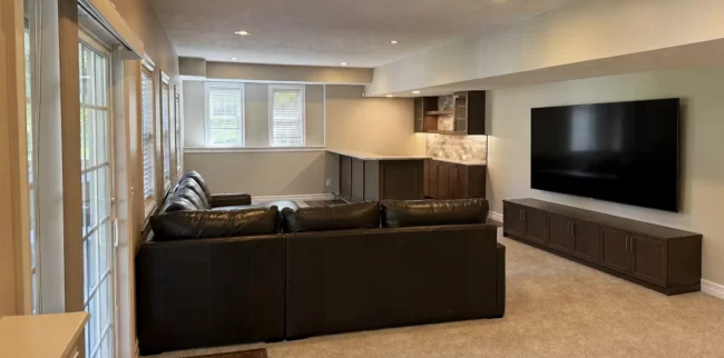 Basement Finishing Overview | Pennings Handyman Finished basement living area with leather sectional, wet bar, recessed lighting, carpet, patio doors, and large windows