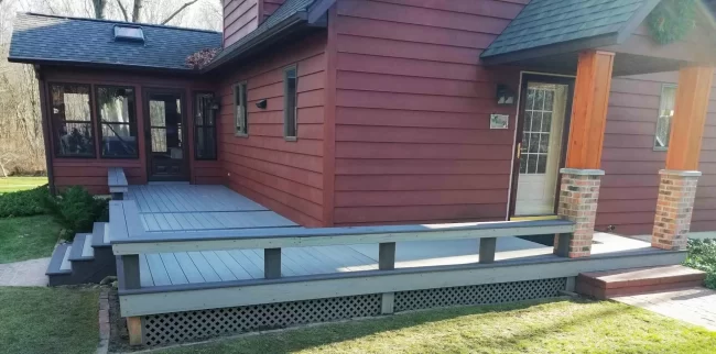 Front Porch Deck Update with Built-In Seating | Pennings Handyman Updated front porch deck with gray decking, built-in bench seating, lattice skirting, and steps leading to the home entry