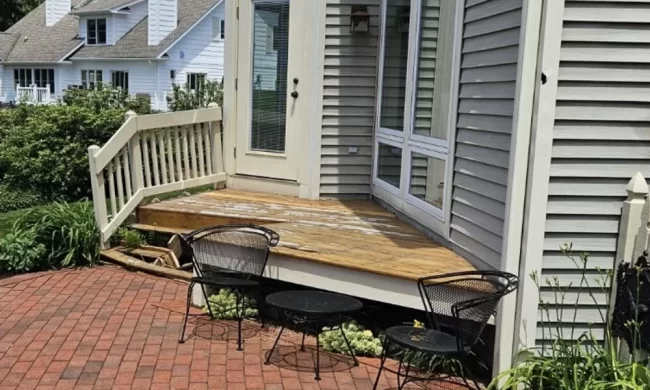 Before view of weathered backyard deck with worn deck boards, older railing, patio furniture, and brick patio below