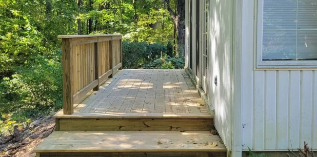After view of newly rebuilt wood deck with fresh deck boards, steps, and railing along the side of the home