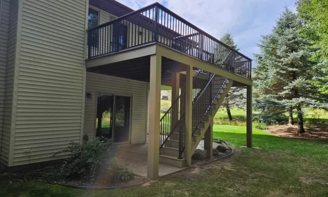 kalamazoo-elevated-deck-after-replacement-aspect-ratio-1000-600 Finished elevated deck replacement with composite decking, black railing, stairs, and support posts overlooking a backyard