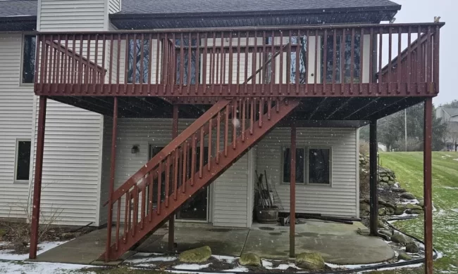 Before photo of an older elevated wood deck with red railing, stairs, and support posts prior to replacement