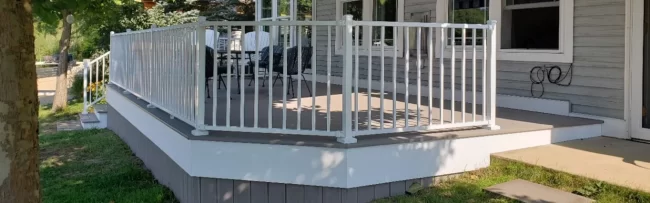 New outdoor deck with white railing, gray decking, and patio seating along the back of a home