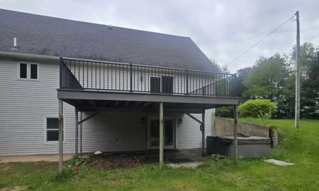 Lawton After photo of a replaced elevated backyard deck with gray composite decking, black railings, support posts, and a covered patio area below