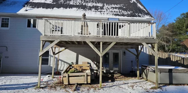 Before photo of an aging elevated backyard deck with weathered wood decking, white railings, exposed support posts, and snow-covered yard below