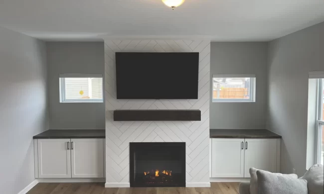 mattawan-after-living-room-fireplace-built-in-as-scaled-aspect-ratio-1000-600 After photo of a living room feature wall with a herringbone fireplace surround, dark wood mantel, mounted TV, and white built-in cabinets