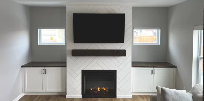 mattawan-after-living-room-fireplace-built-ins-a-scaled-aspect-ratio-1920-950 After photo of a living room feature wall with a herringbone fireplace surround, dark wood mantel, mounted TV, and white built-in cabinets