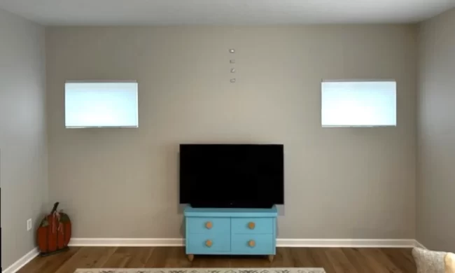 Before photo of a plain living room wall with small windows and a TV cabinet before the fireplace feature wall and built-in storage