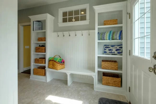 mudroom-bench-cubbies-with-storage-1-aspect-ratio-960-640 White built-in mudroom cubbies with bench seating, coat hooks, open shelves, and wicker storage baskets