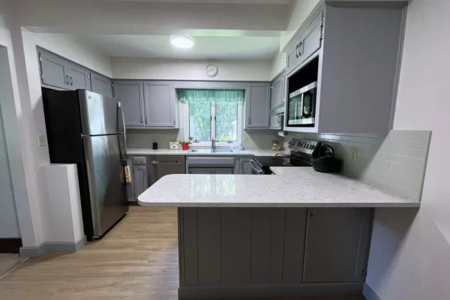 refacing-kitchen-cabinets-1-aspect-ratio-960-640 Refaced kitchen with freshly painted gray cabinets, updated countertops, backsplash, and light wood flooring