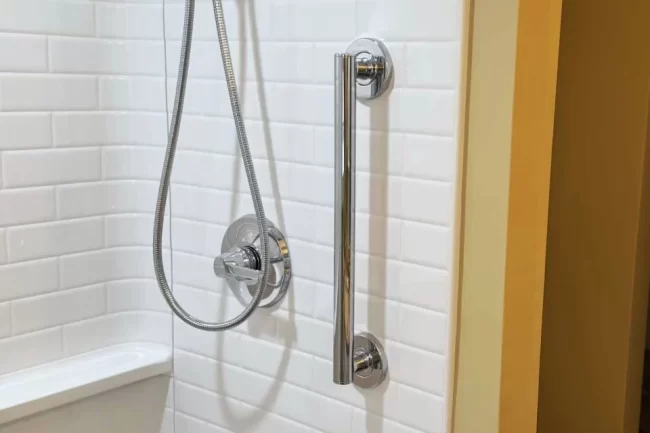 shower-grab-bar-installation-aspect-ratio-960-640 Chrome grab bar installed on a white subway tile shower wall next to updated shower fixtures