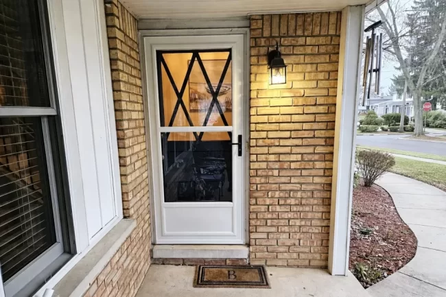 White storm door installed on a covered brick front porch with black hardware and exterior lighting